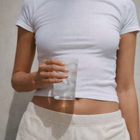 Hand holding a clear glass of water with ice cubes against a neutral, minimal background